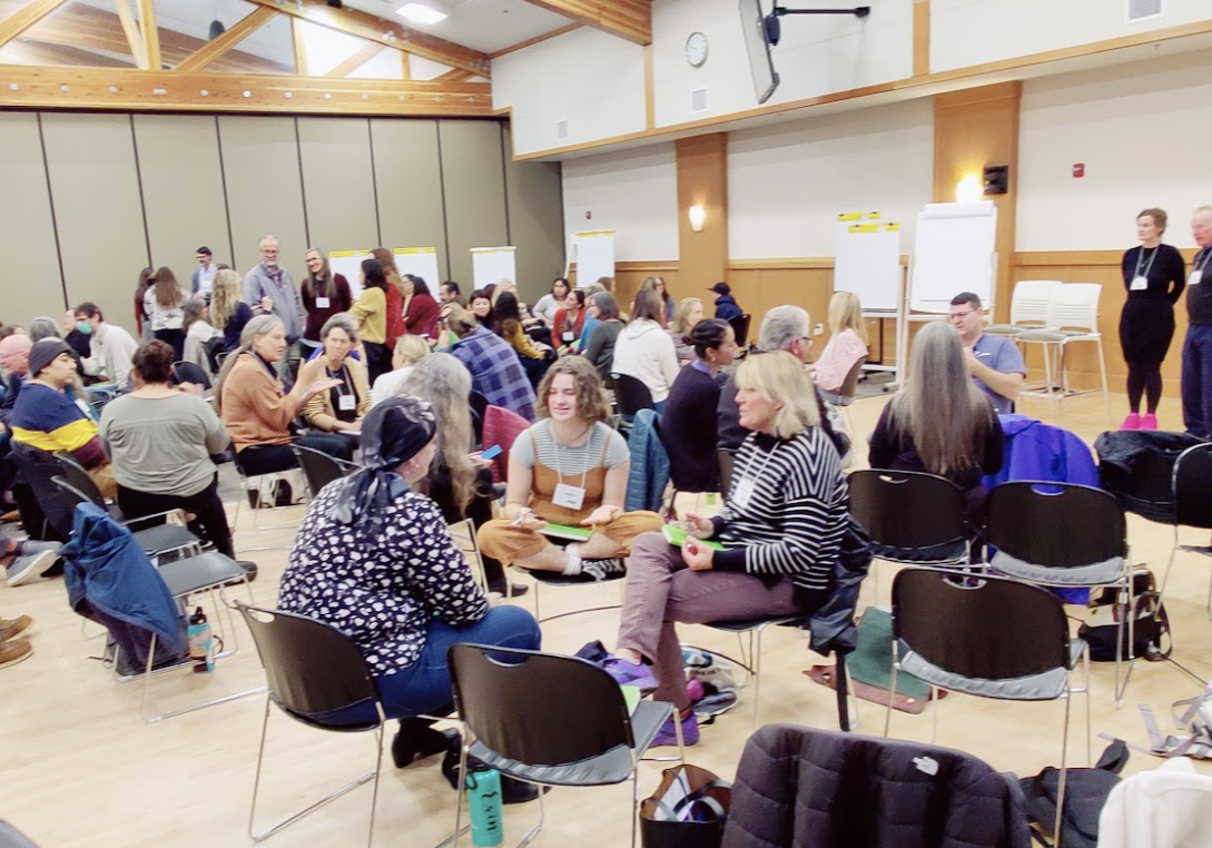 Group of people sitting and speaking with one another in small circles in chairs.